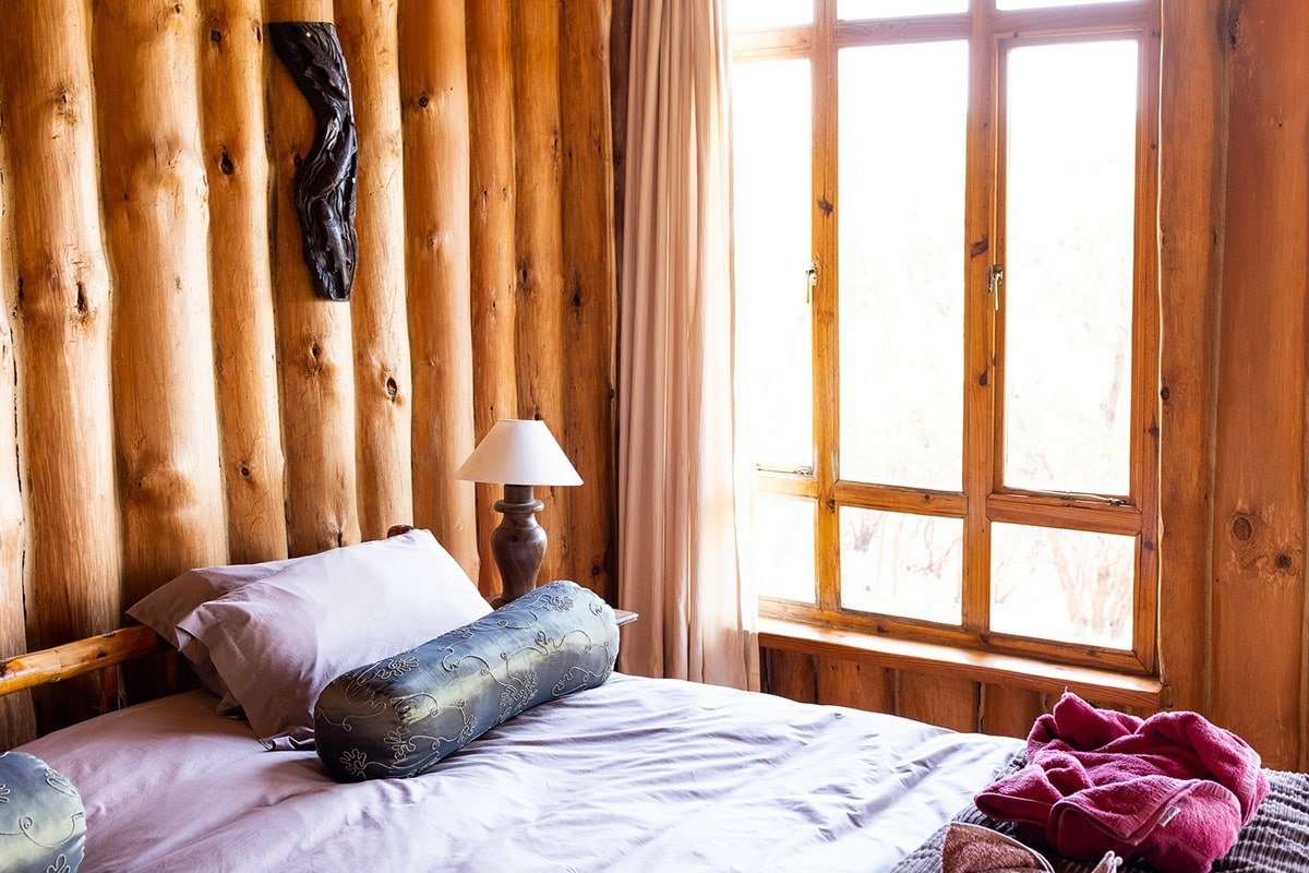 A log-walled bedroom with a lamp and garden view at Chelinda Lodge